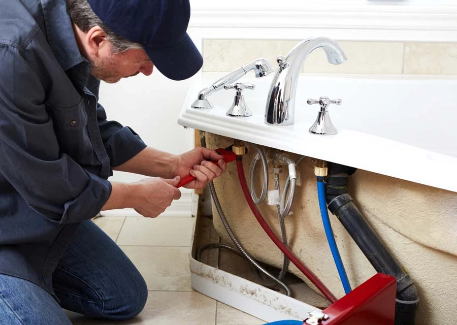 Plombier professionnel à genoux dans une salle de bain moderne, intervenant sous un lavabo blanc avec robinetterie chromée