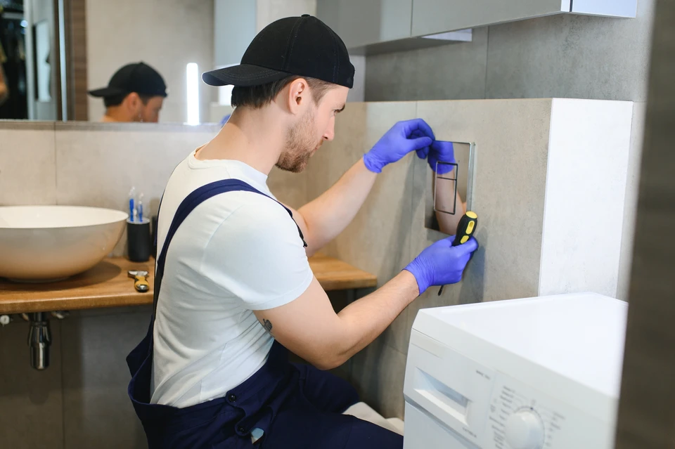 Plombier professionnel en combinaison de travail et gants bleus installant ou réparant une chasse d'eau dans une salle de bains moderne