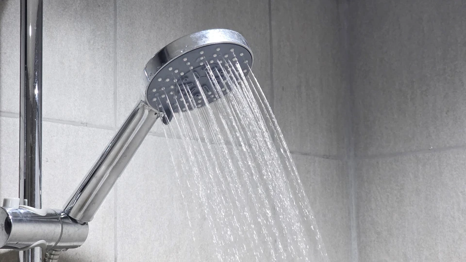 Plombier intervenant sous un chauffe-eau, manipulant une pince sur les raccordements hydrauliques